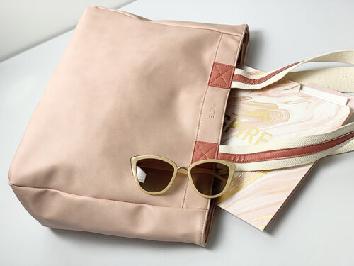close up of coral bag with darker coral and white stripe straps on white desk with journal and sunglasses