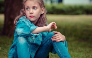 Scared, sad child sitting on grass in blue jeans and jean jacket