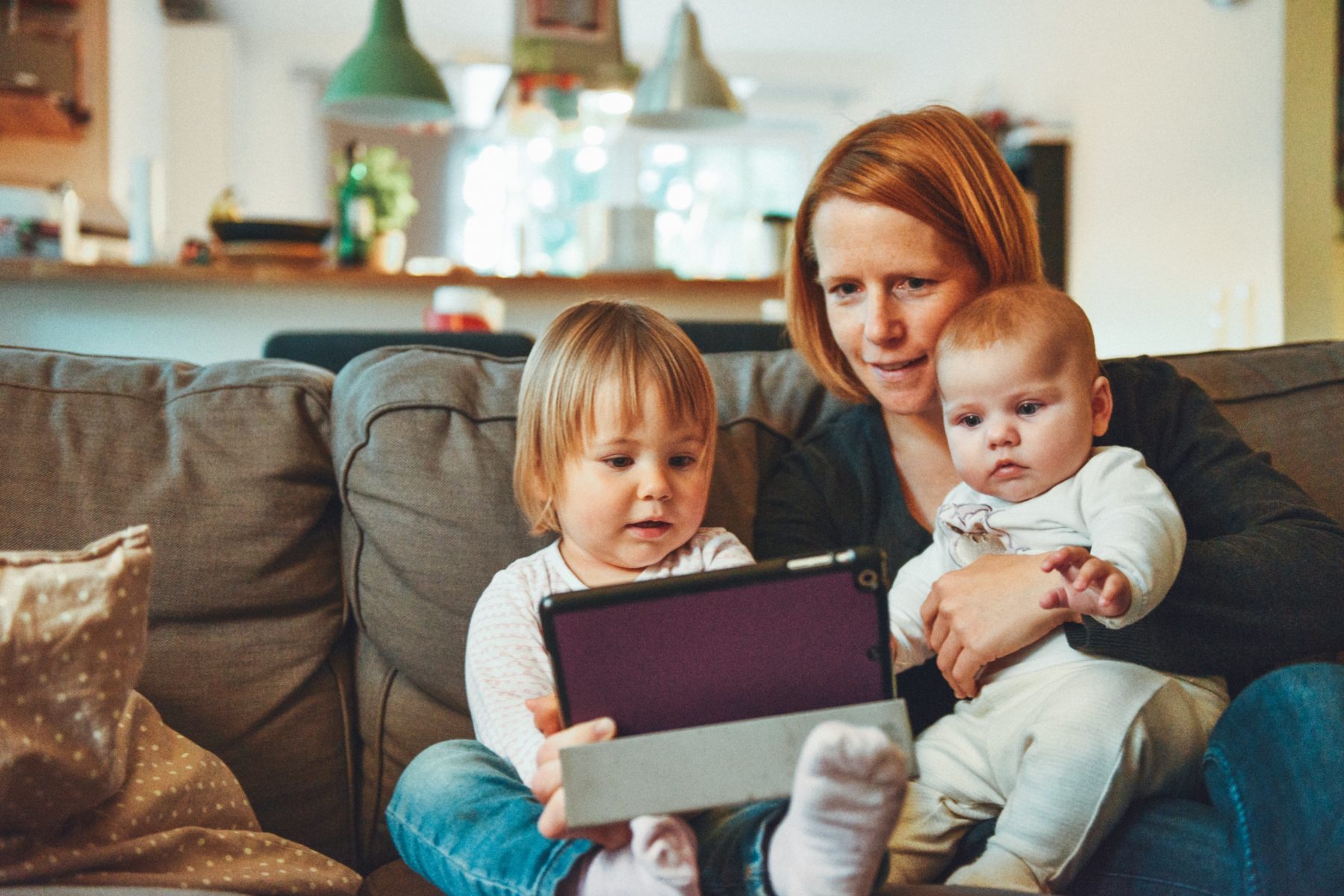 Mother with baby and toddler on couch looking at tablet
