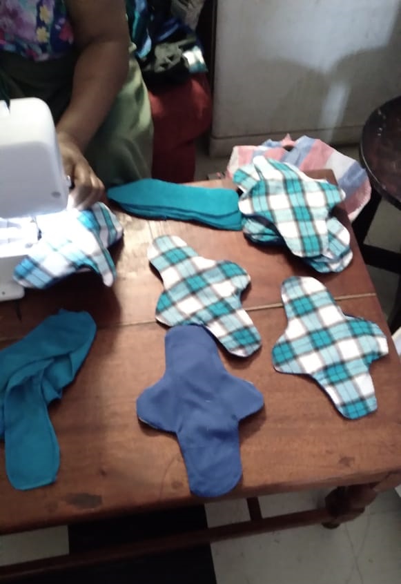 Blue and plaid fabric shaped like sanitary napkins on a brown table next to a sewing machine